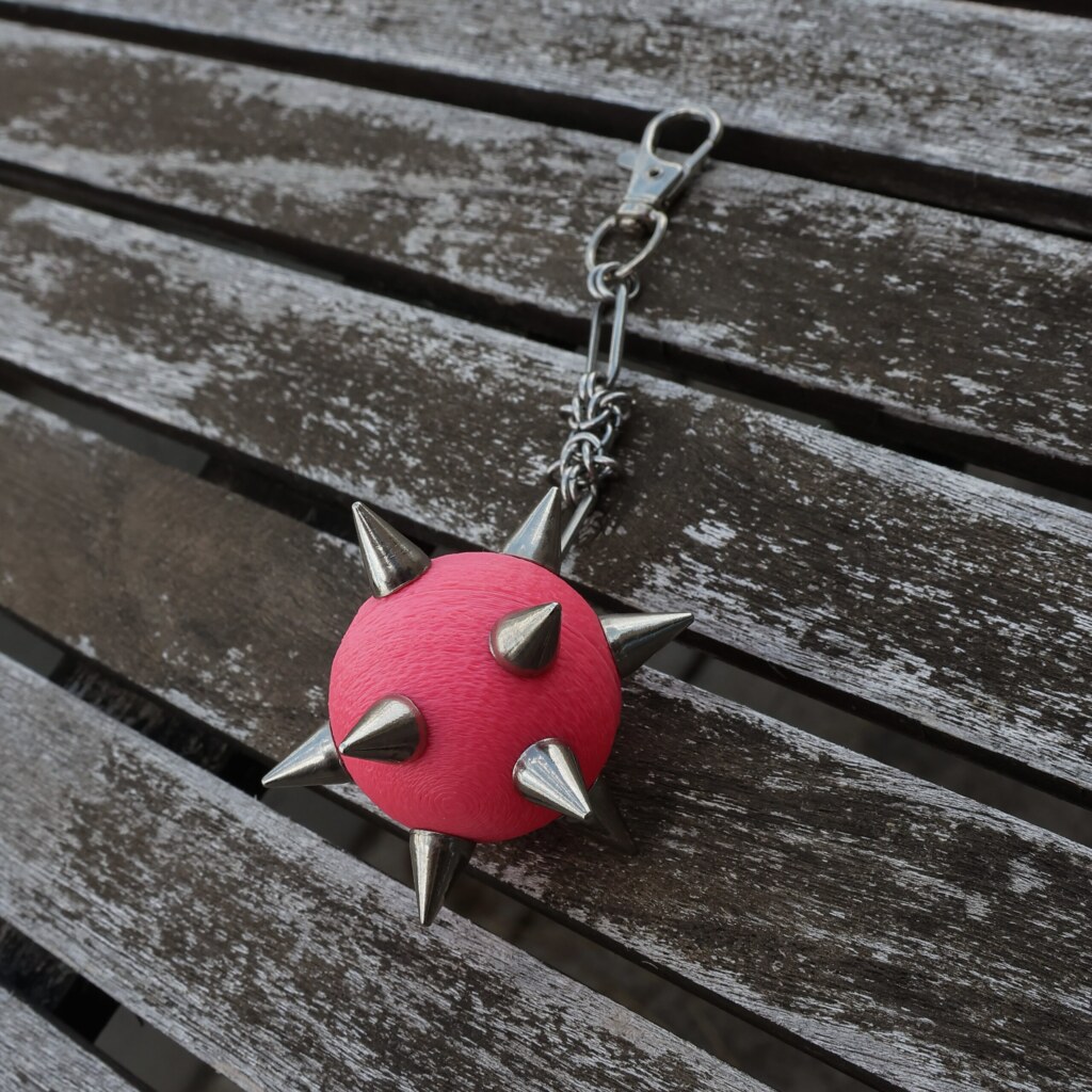 Handmade bag charm with a rosa spiked ball pendant and stainless steel paperclip chain, lying on an table.