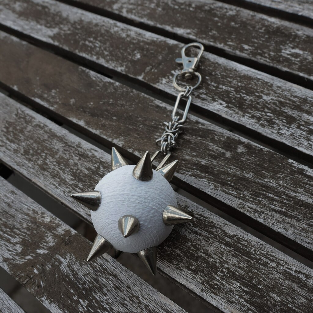 Handmade bag charm with a white spiked ball pendant and stainless steel paperclip chain, lying on an table.
