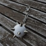 Handmade bag charm with a white spiked ball pendant and stainless steel paperclip chain, lying on an table.