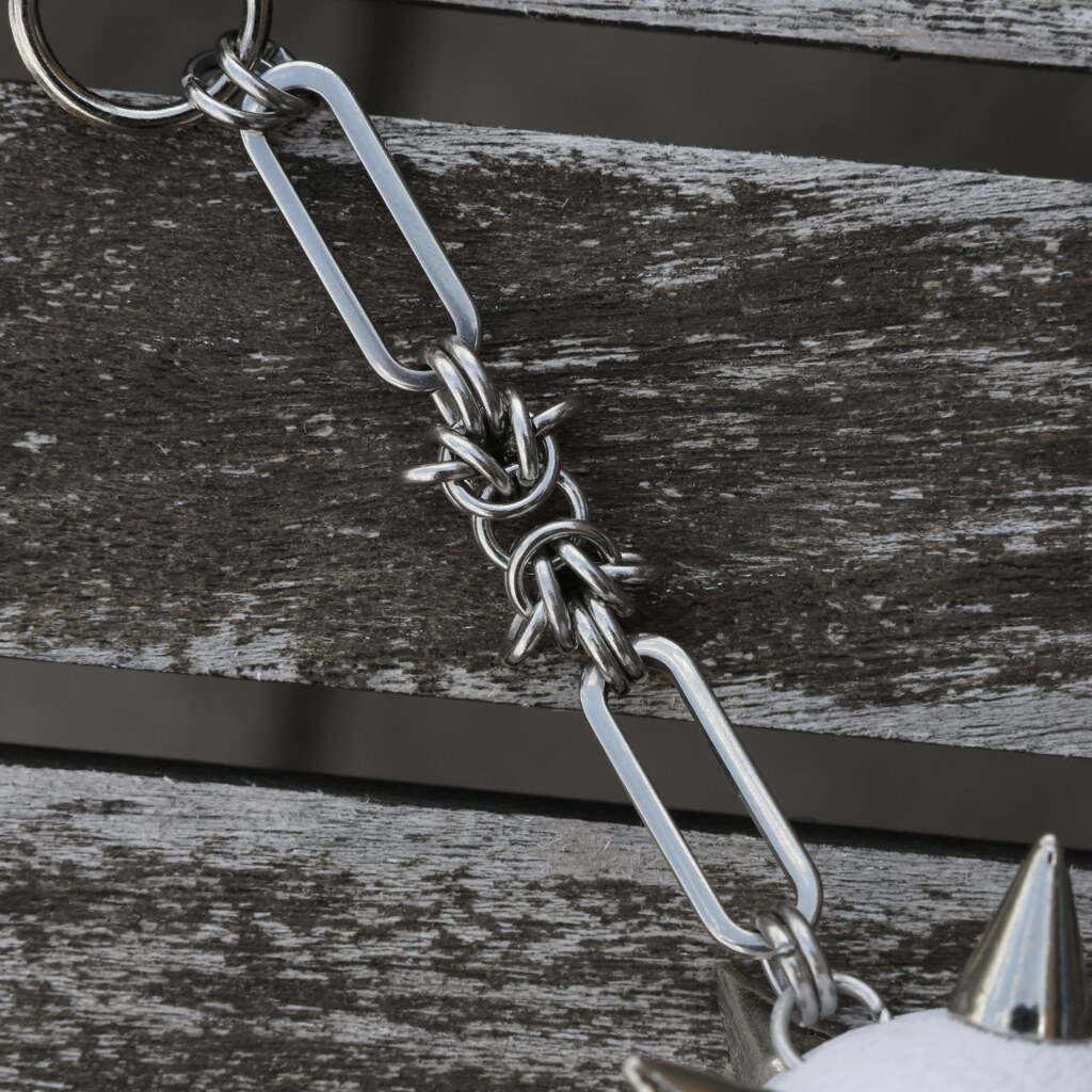 Closeup of the handmade chainmail chain for an bag charm with a spiked ball pendant and stainless steel paperclip chain, lying on an table.