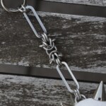 Closeup of the handmade chainmail chain for an bag charm with a spiked ball pendant and stainless steel paperclip chain, lying on an table.